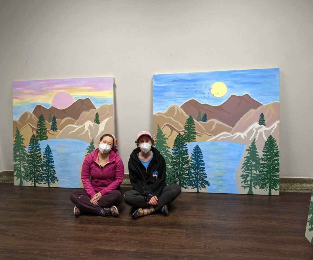 Bareket and Amanda sit between two landscape murals