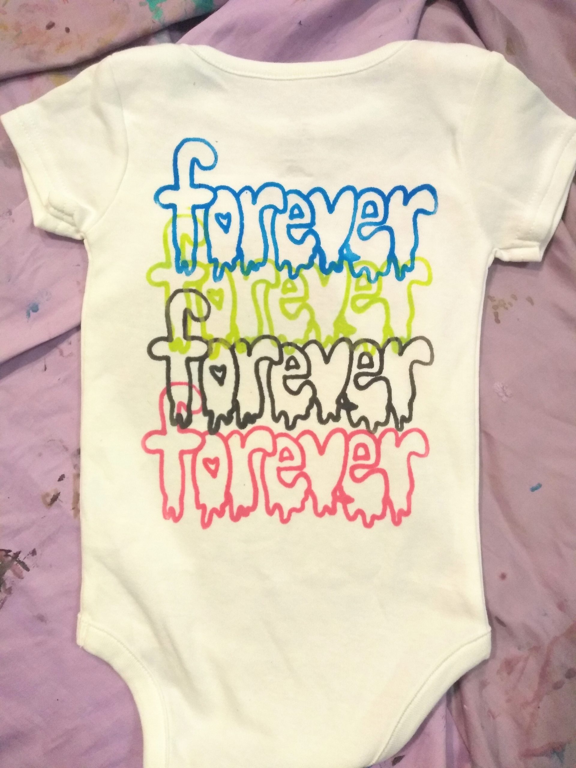 Baby onesie with coloured repeated text on top of each other reads forever