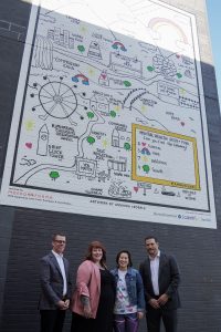 Four people standing in front of large black and white mural with spots of colour on black wall to celebrate mental health artwork in Toronto.