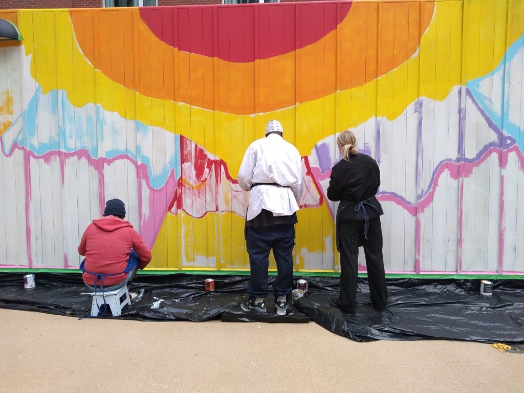 Back of 3 people painting a large fence
