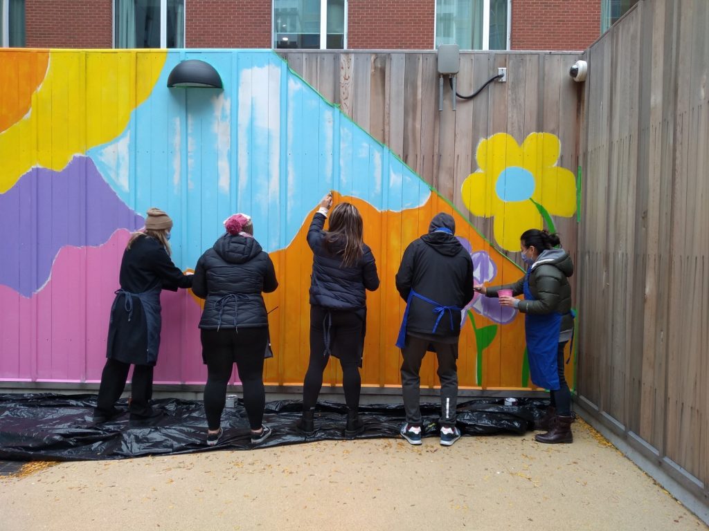 The back of five people as they paint a colourful fence