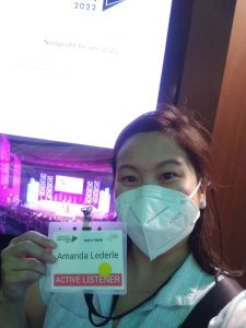 Amanda in mask in front of a bright screen holding name tag
